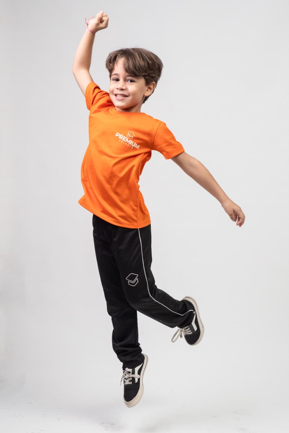 Criança do Fundamental I saltando de alegria com o uniforme laranja do PREMIUM