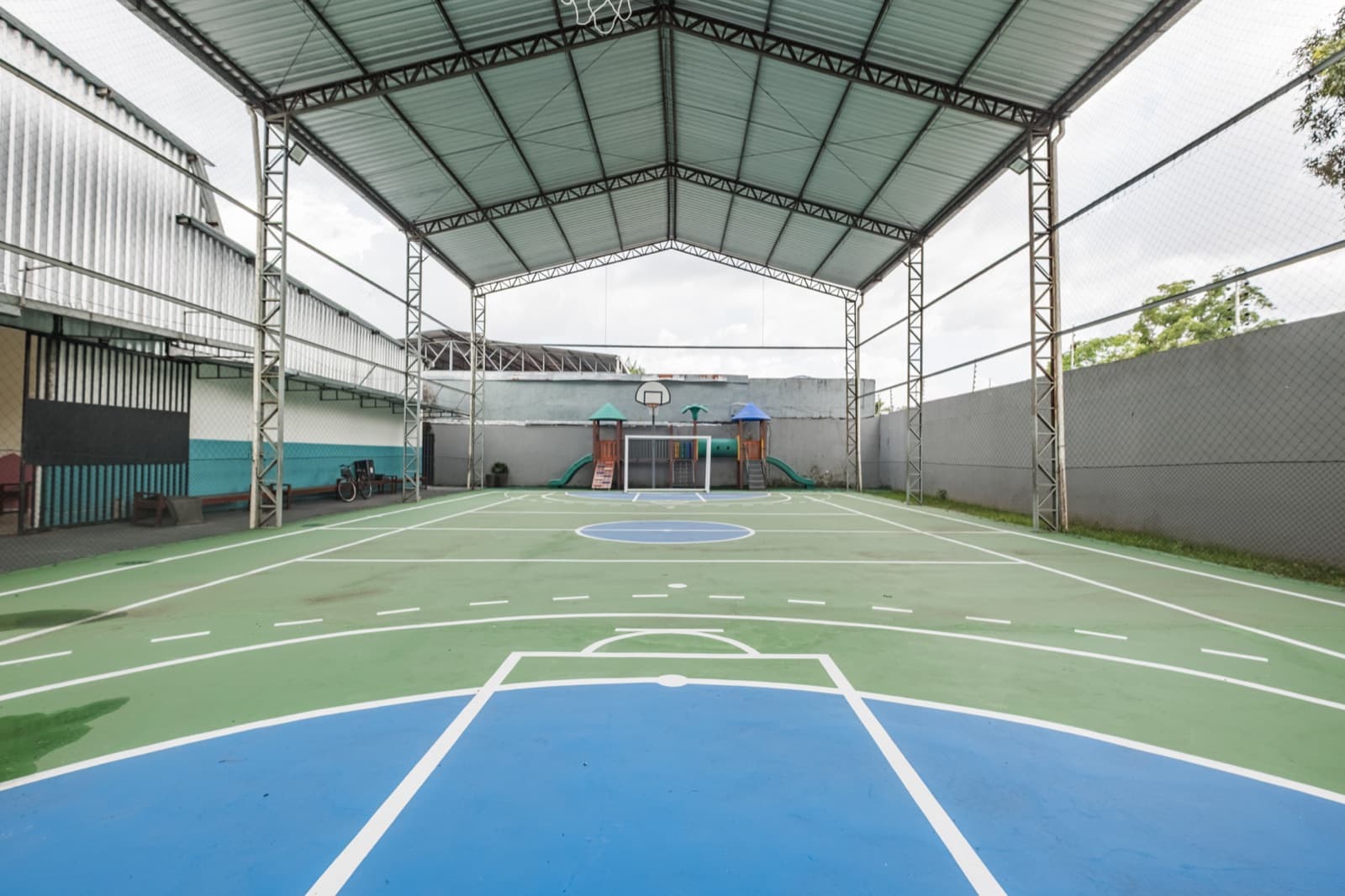 Quadra poliesportiva coberta com playground ao fundo